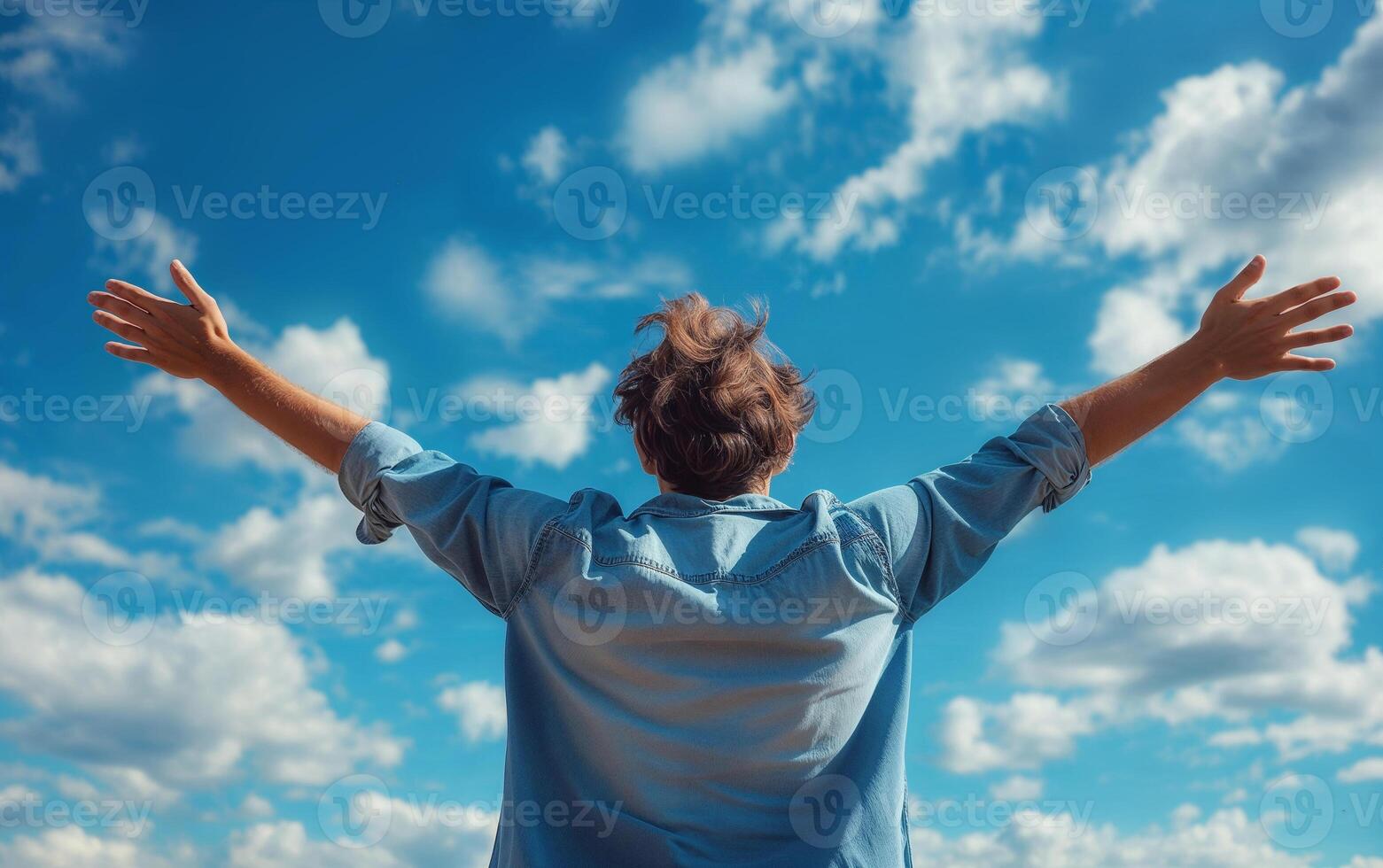 Back view of a person with arms wide open against a vibrant blue sky, expressing freedom photo