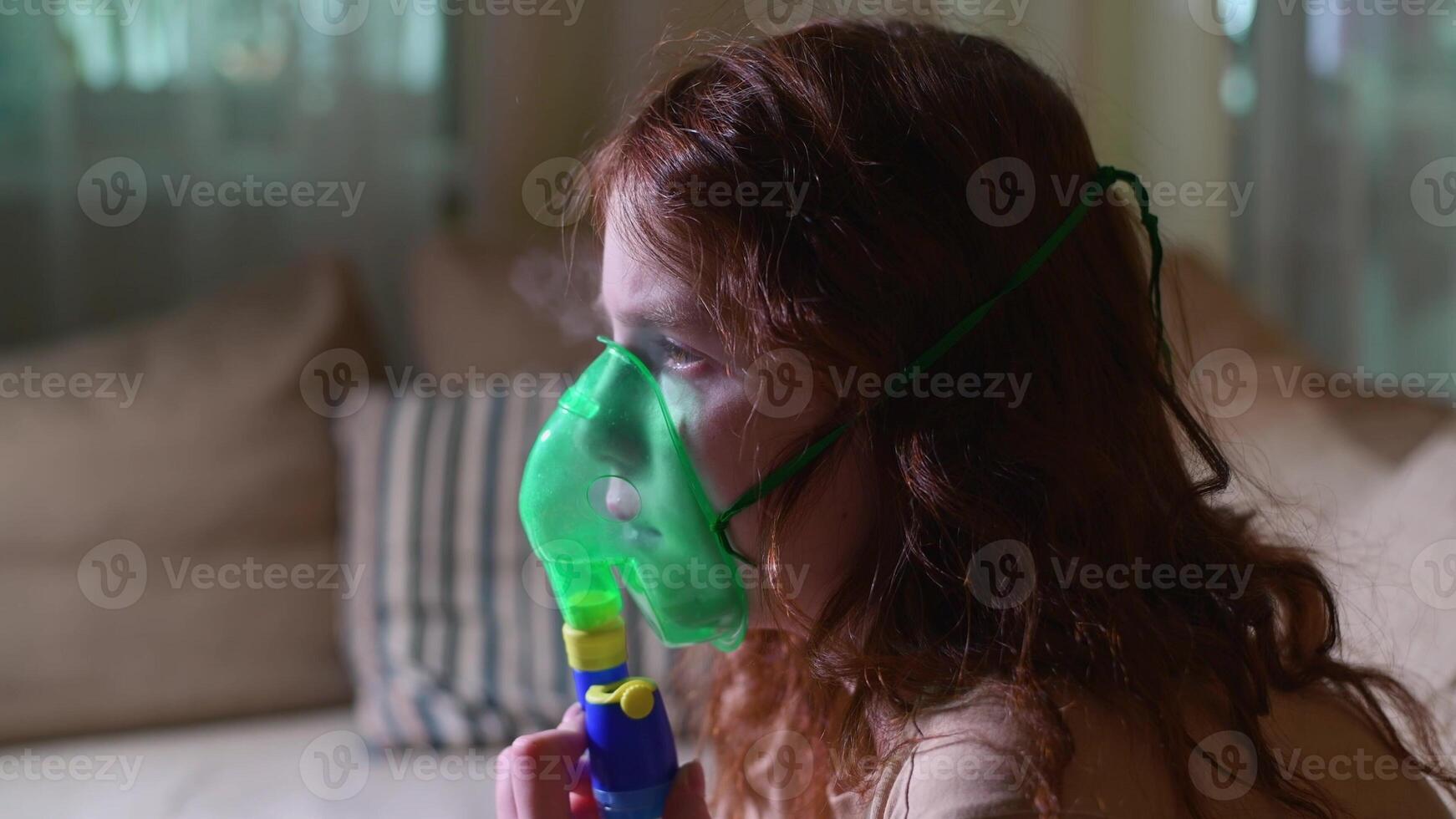 Sick girl making inhalation with nebulizer to reduce coughing, at home, child taking medication while breathing in through face mask. Bronchitis and asthma treatments for children photo