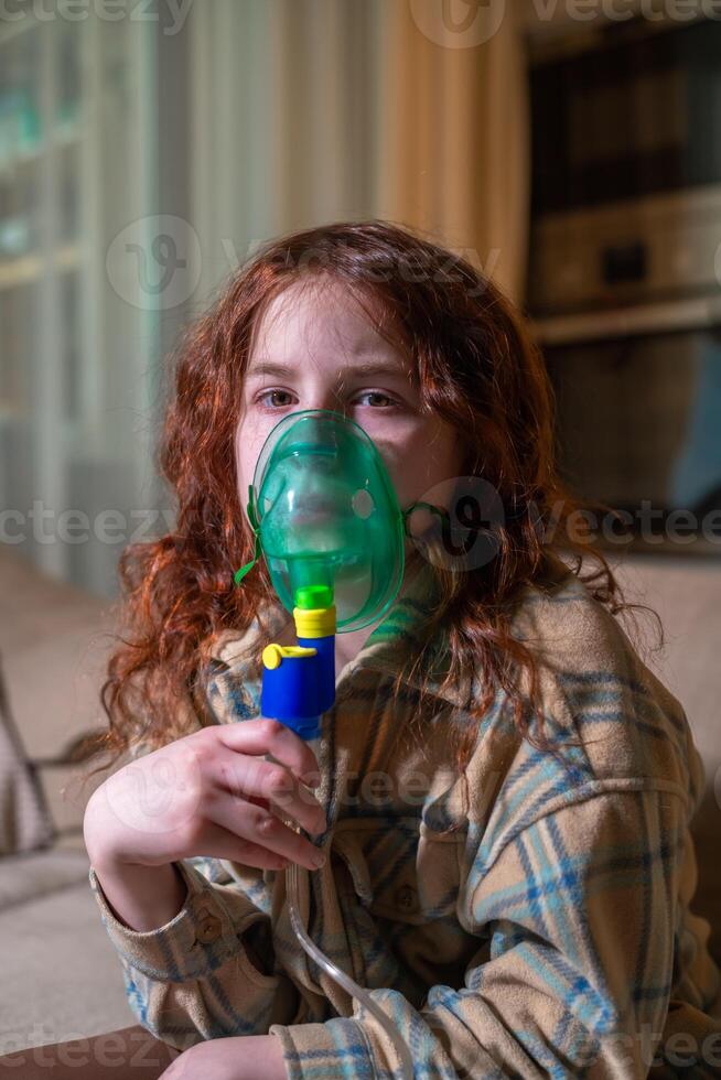 Sick girl making inhalation with nebulizer to reduce coughing, at home, child taking medication while breathing in through face mask. Bronchitis and asthma treatments for children photo