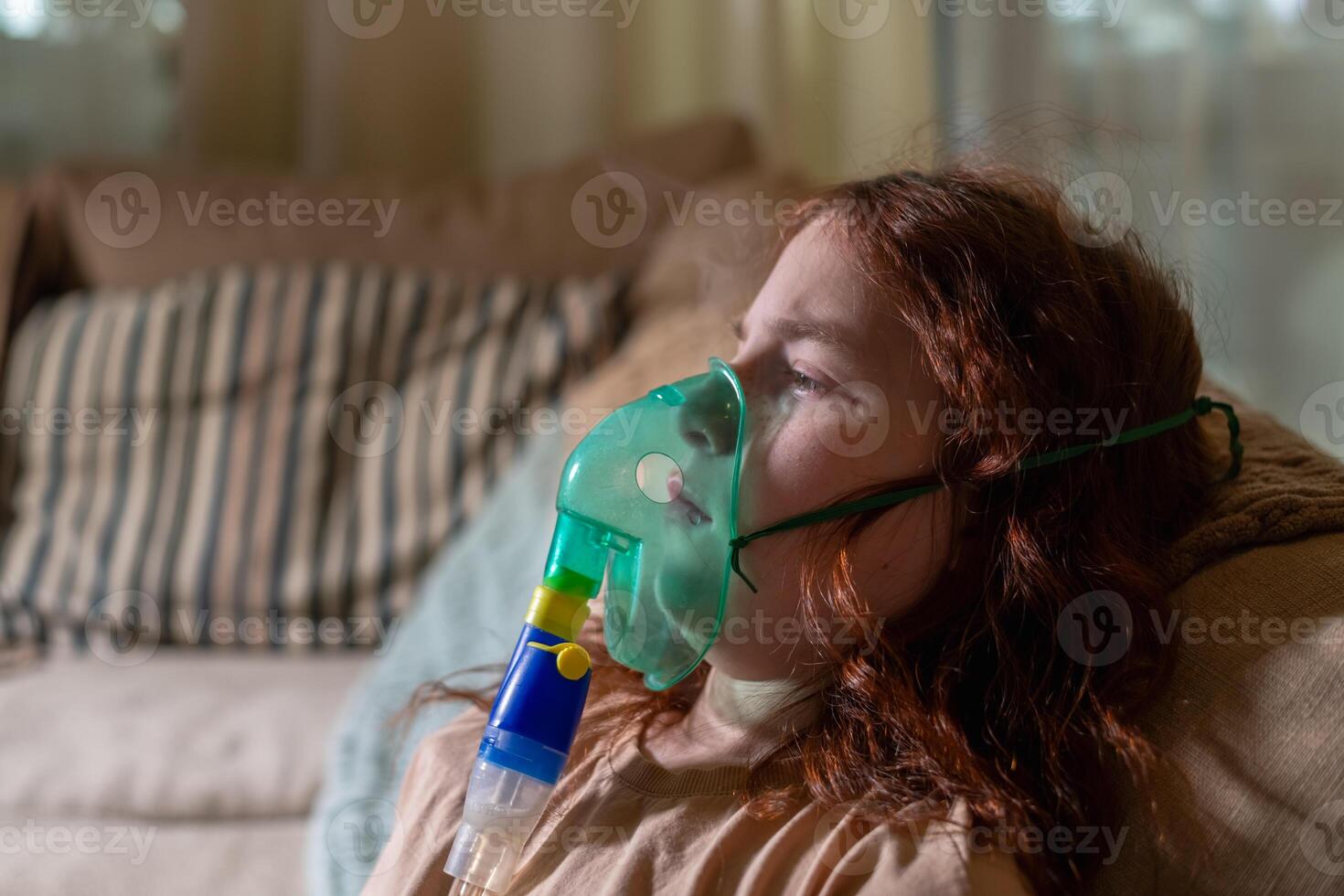 Sick girl making inhalation with nebulizer to reduce coughing, at home, child taking medication while breathing in through face mask. Bronchitis and asthma treatments for children photo