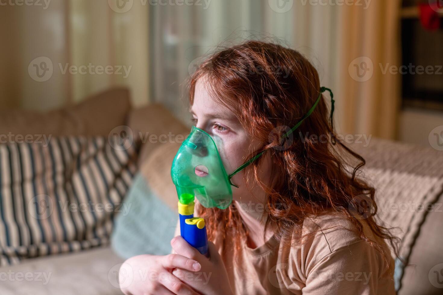 Sick girl making inhalation with nebulizer to reduce coughing, at home, child taking medication while breathing in through face mask. Bronchitis and asthma treatments for children photo