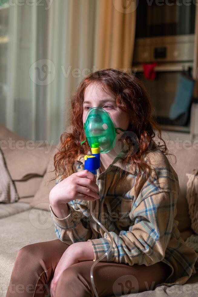 Sick girl making inhalation with nebulizer to reduce coughing, at home, child taking medication while breathing in through face mask. Bronchitis and asthma treatments for children photo