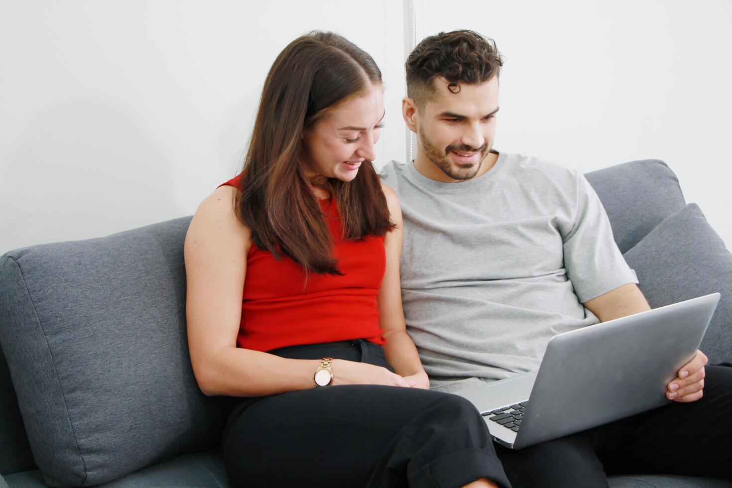 Smiling Caucasian Couple sitting on sofa and working for online business on laptop in social media technology. Work from home and Covid 19 virus is spreading around the world Concept. photo