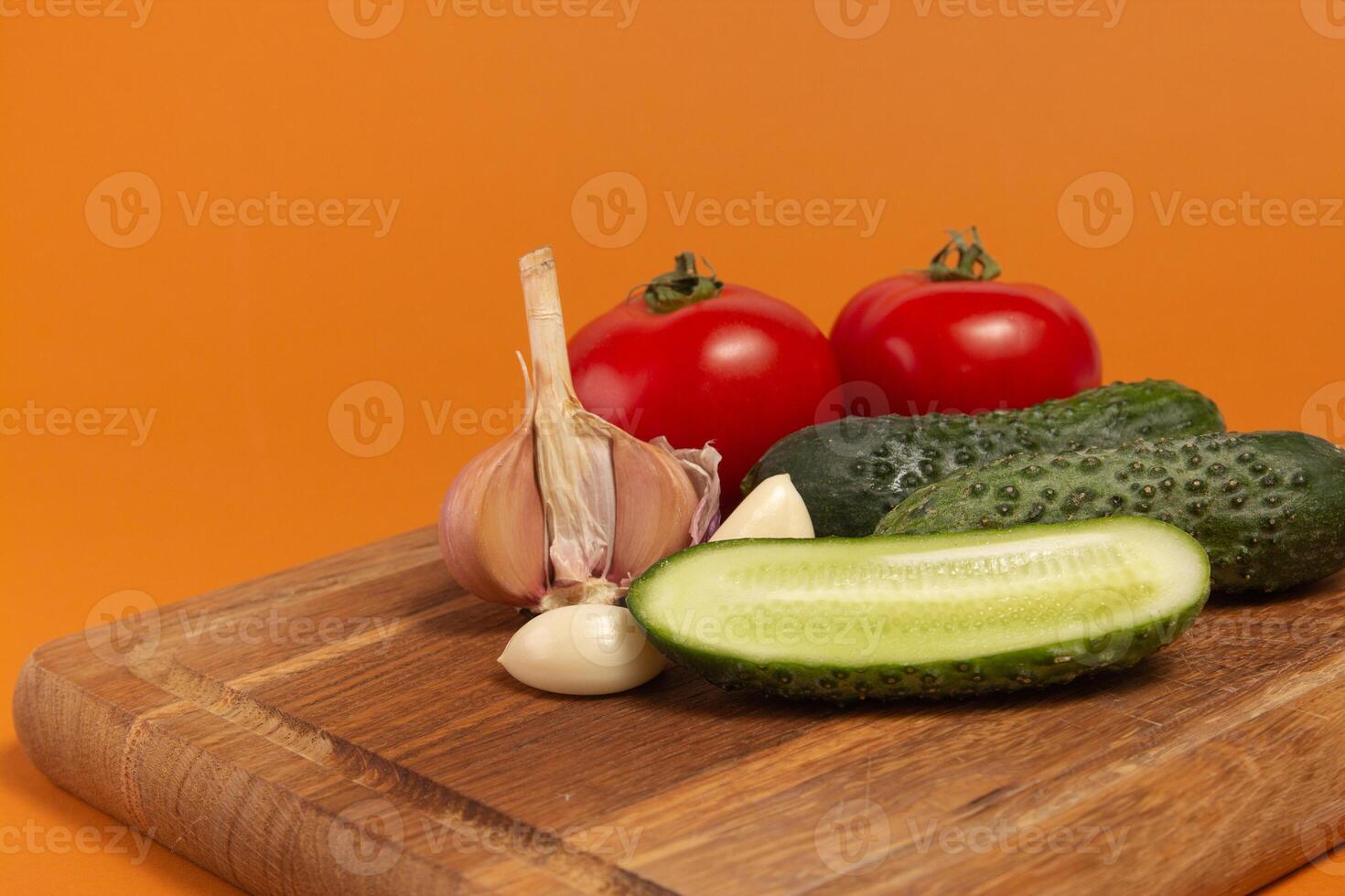 Sliced cucumber, tomatoes and garlic on wooden cutting board. Tomatoes with green ponytails. Healthy food. Copy space. High quality close-up photo