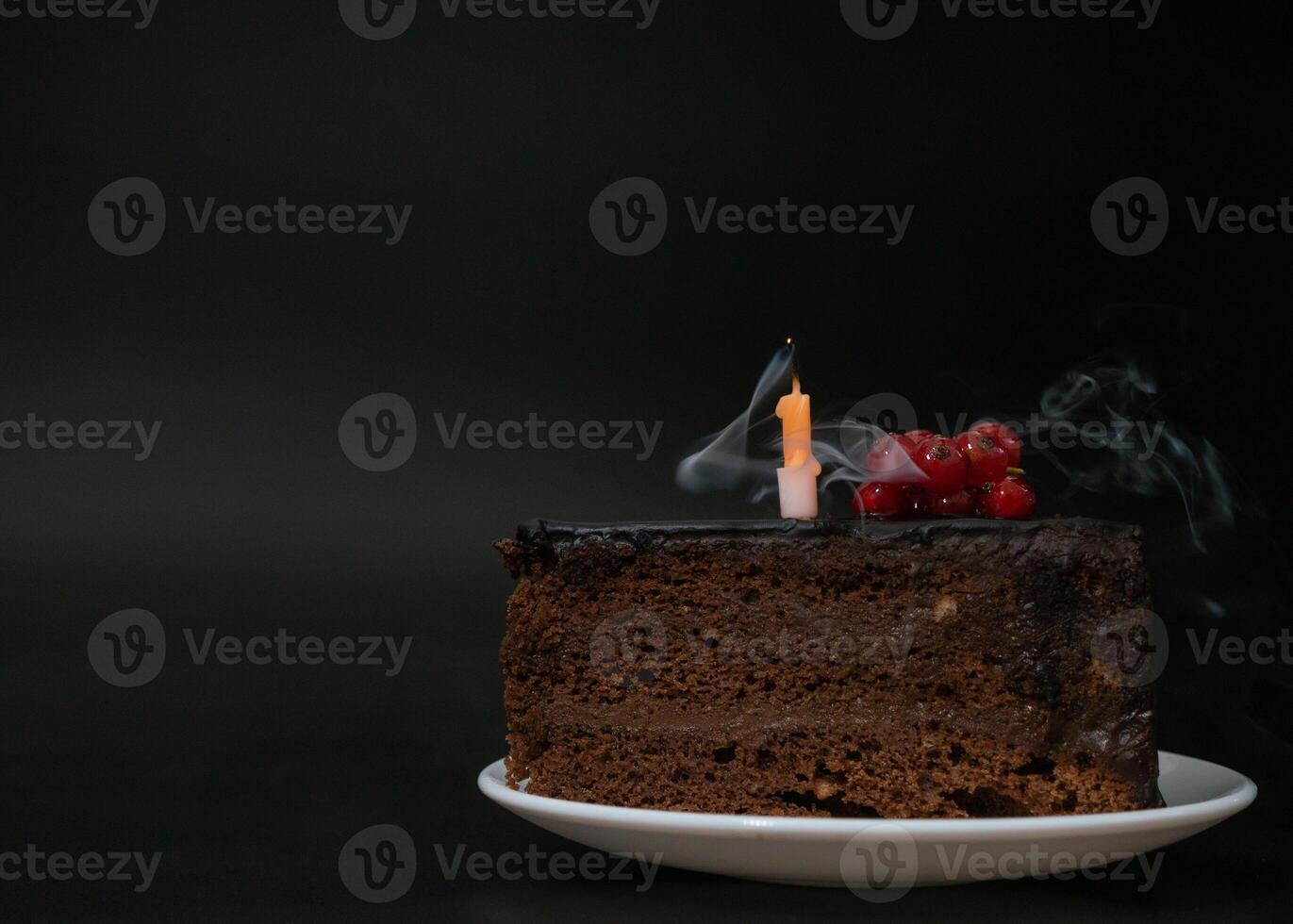 Piece of chocolate birthday cake with one extinguished candle on white plate on deep black background. Birthday party, celebration, anniversary. Close-up, copy space for your text. photo
