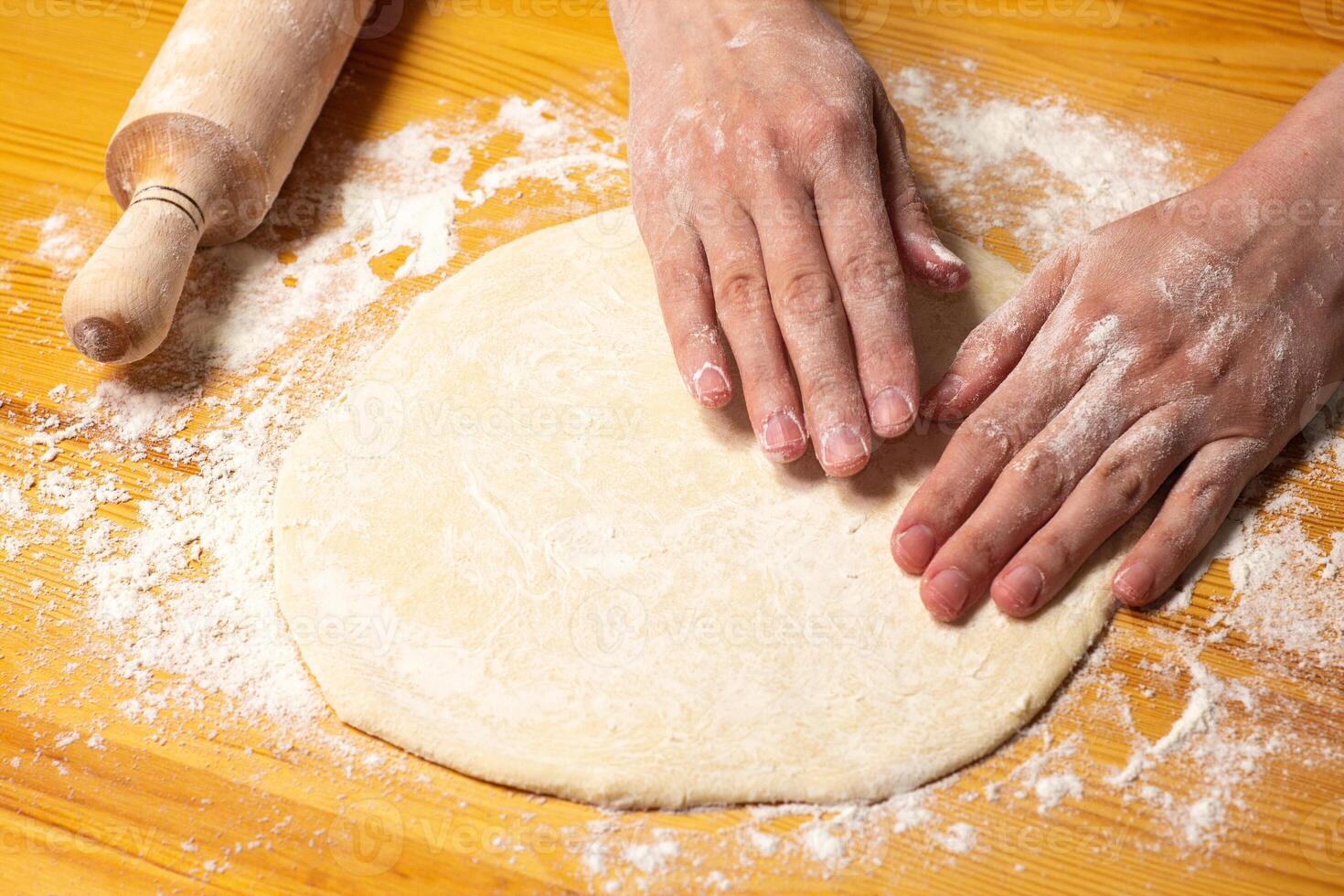 Hands with rolling-pin make dough for pizza. Italian pizza cooking preparation process on wood table. Pizza dough photo