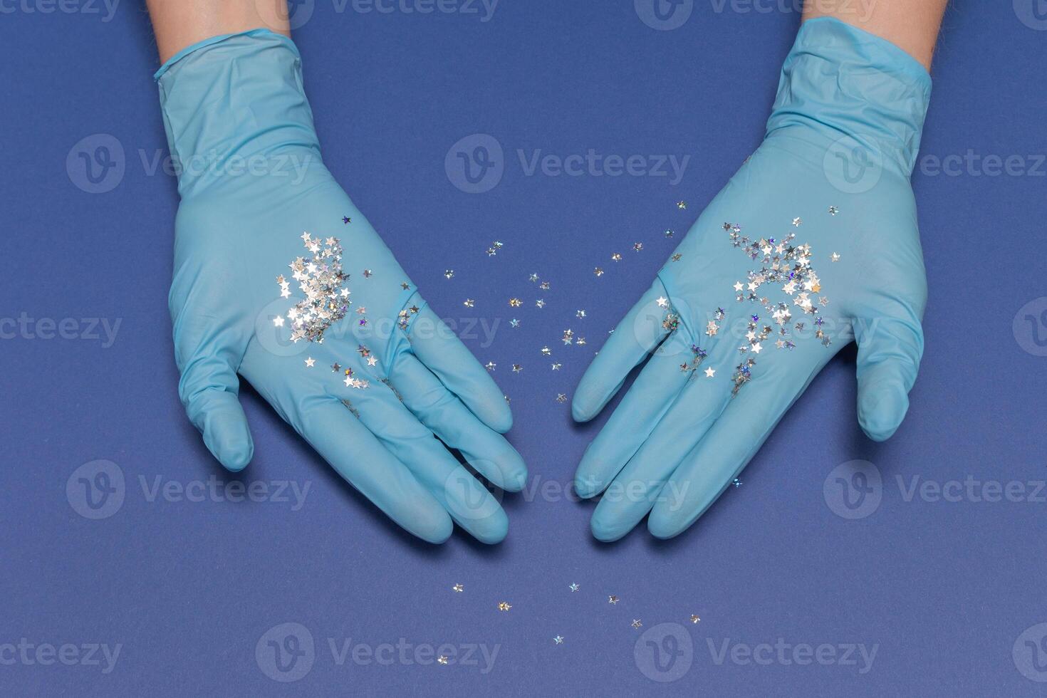 Hands in medical gloves on blue background. Glitter little stars in hands. Christmas and New Year card concept. Top view photo, copy space. photo