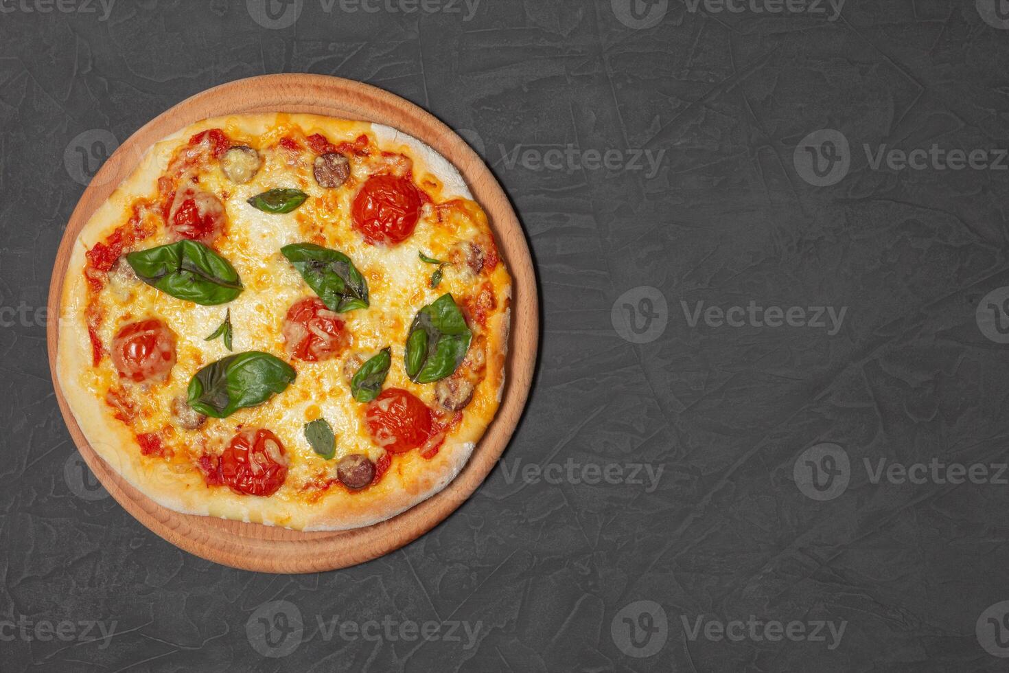 Pizza on wooden plate on black stone background. Cheese pizza with tomato, mozzarella and basil. Close-up photo. Copy space. photo