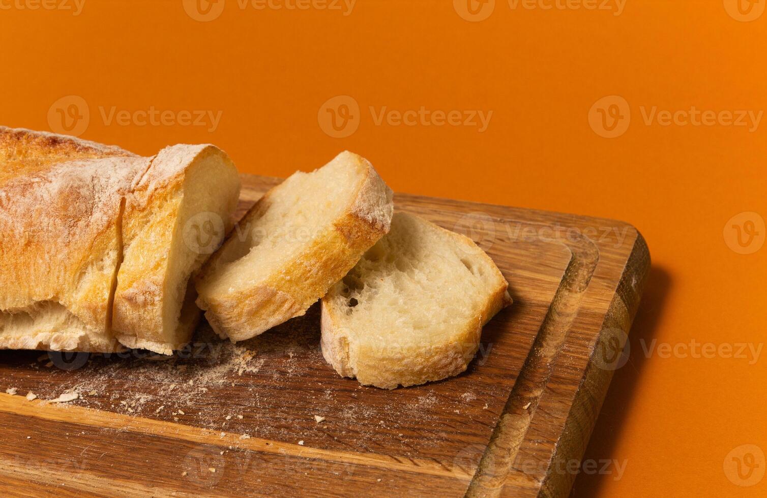 Sliced bread baguette on a wooden cutting board on a terracote color background. Close up high quality photo. photo