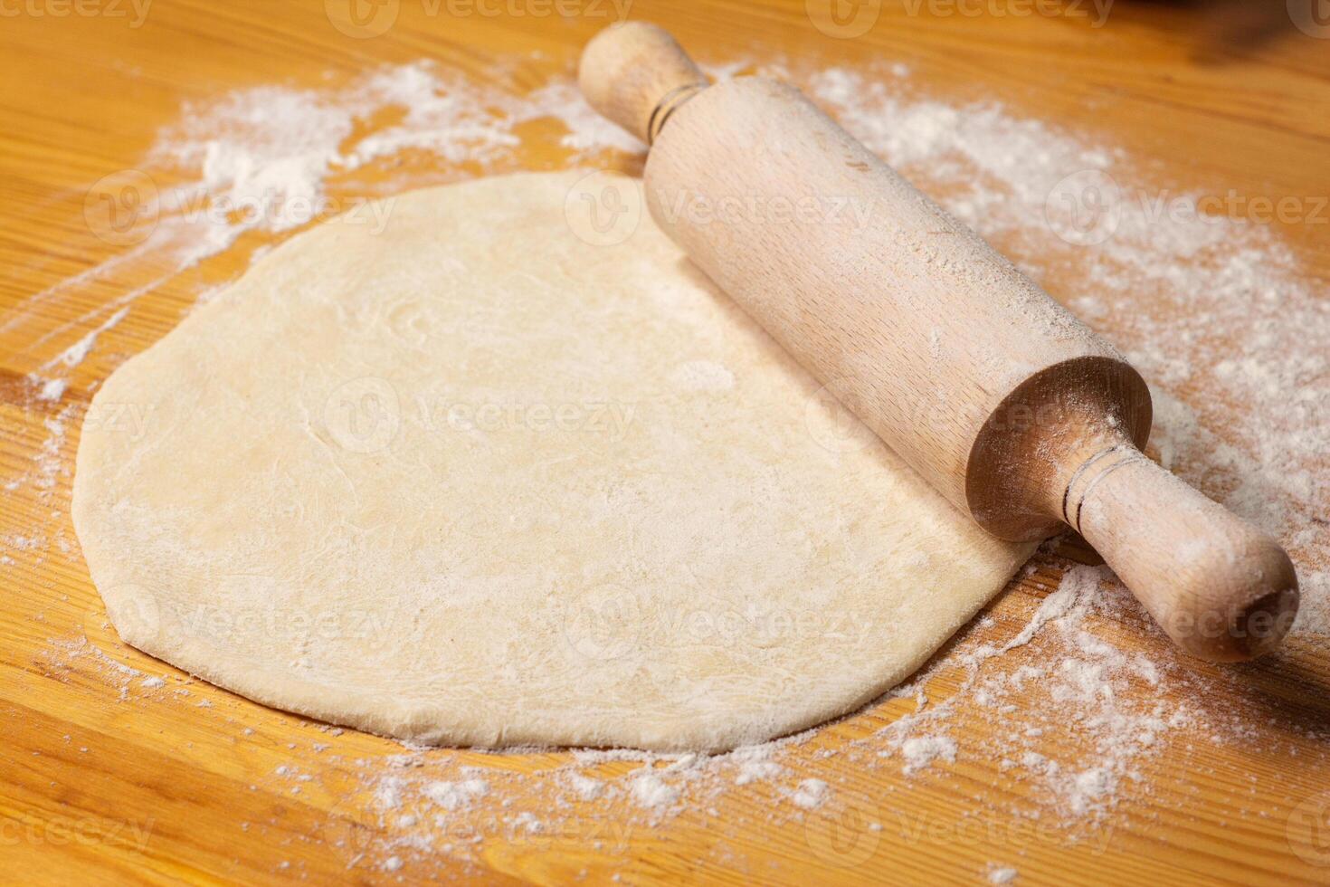 Pizza dough on wooden background. Rolling-pin and flour. Selective focus photo