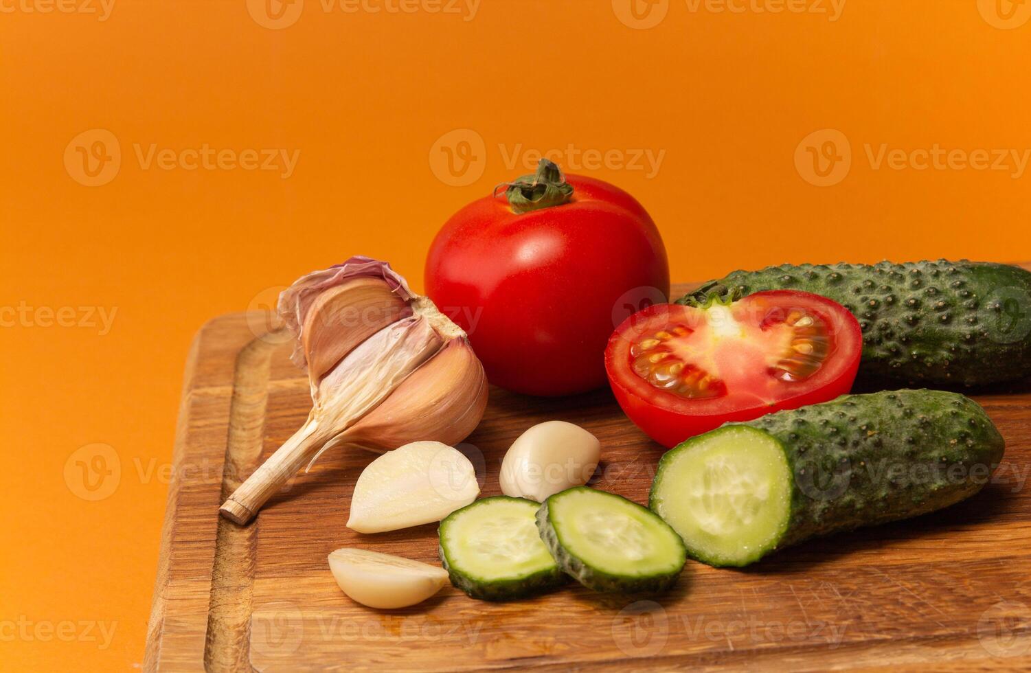 Sliced cucumber, tomatoes and garlic on wooden cutting board. Tomatoes with green ponytails. Healthy food. Copy space. High quality close up photo
