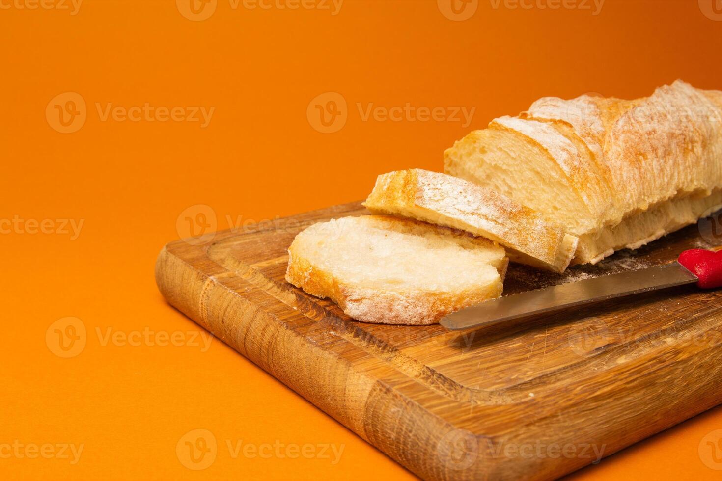 Sliced bread baguette on a wooden cutting board with knife on a terracote color background. Copy space. Close-up high quality photo