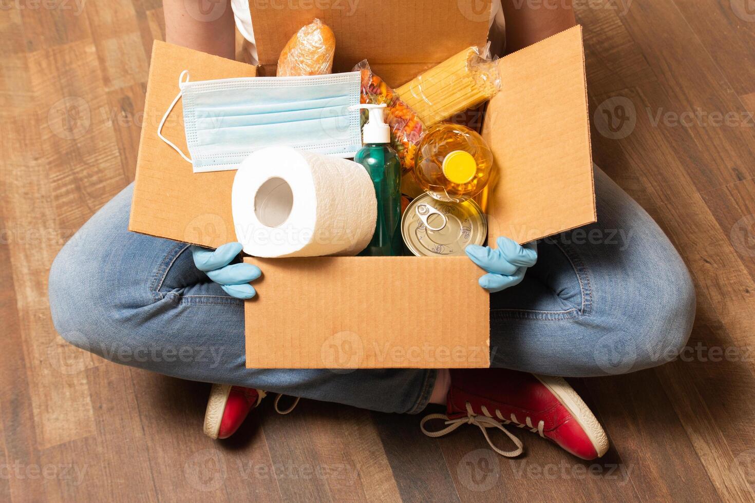 A volunteer has sitting on the floor and holding donation box with food, toilet paper and sanitizer. Food delivery service for those who need. High quality photo