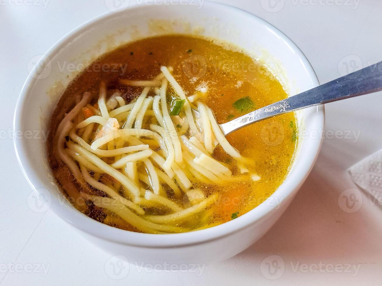 bowl of chicken broth soup with vegetables and vermicelli on white background photo