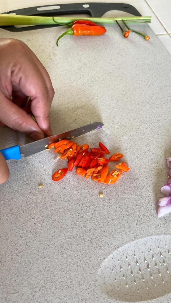 someone cutting up some red peppers on a cutting board with a knife photo