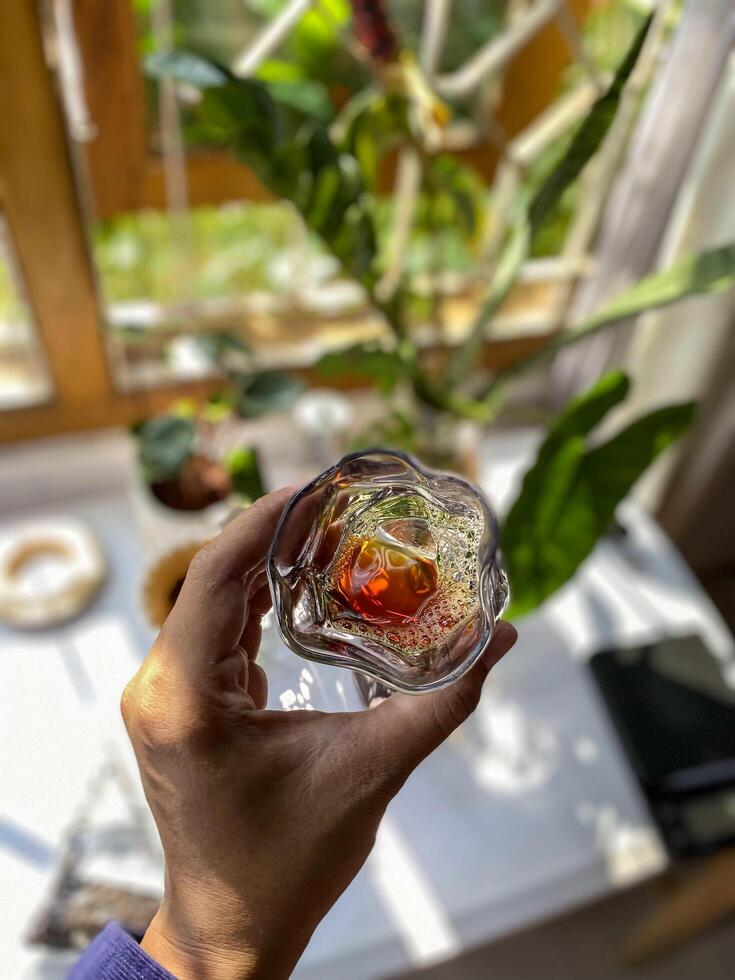 someone holding a glass of coffee in front of a window photo