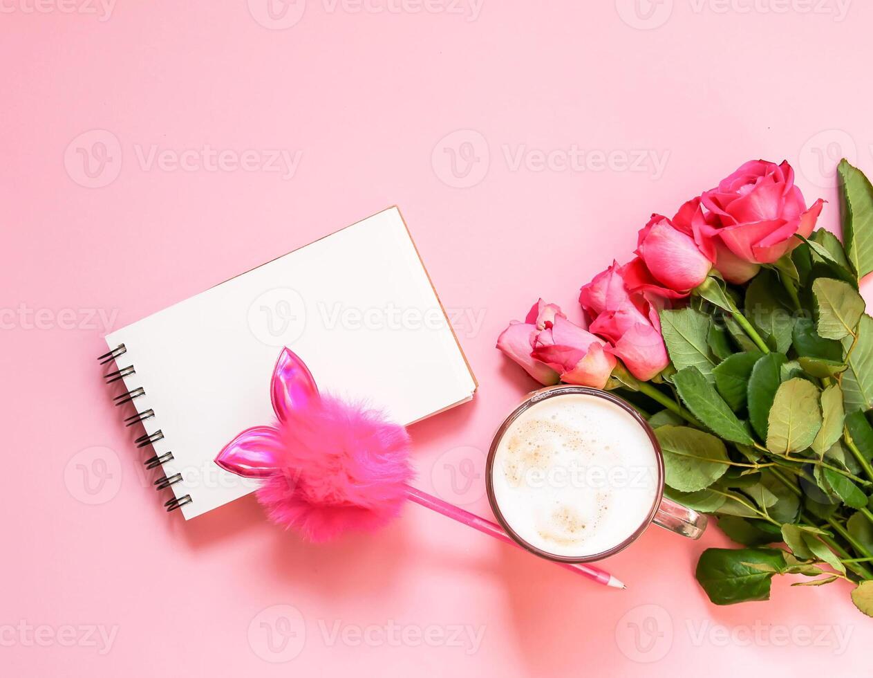 The cup of hot coffee, empty notepad with funny pen and bouquet of fresh roses on soft pink background. photo