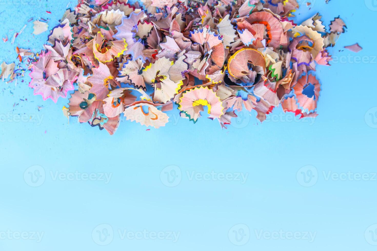 Wooden pencil shavings and colorful crumbs of graphite from sharpener on soft pastel paper background. Top view. Design elements for poster, banner, cards photo