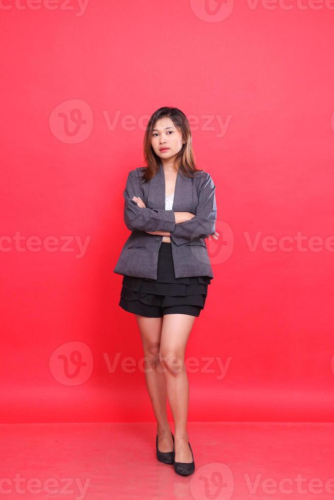Elegant asian girl executive in gray suit with long hair, white skin, taking photo in studio on red background standing with arms crossed. for corporate concepts, fashion and advertising