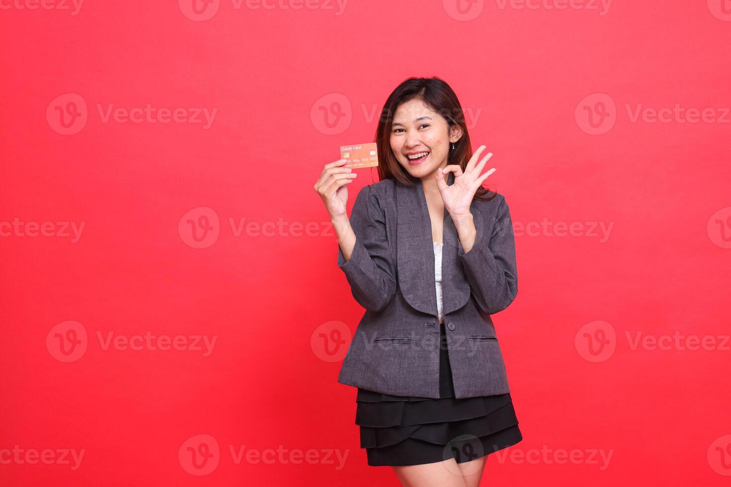 indonesia businesswoman expression happy OK sign ready and holding debit credit card wearing jacket and skirt red background. for financial, business and advertising concepts photo