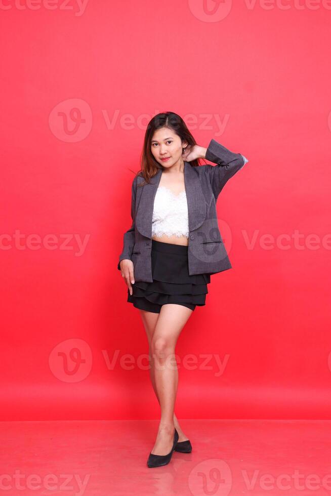 full body asian woman in gray suit looking at camera holding back neck long hair, white skin in studio on red background. for corporate concepts, fashion and advertising photo