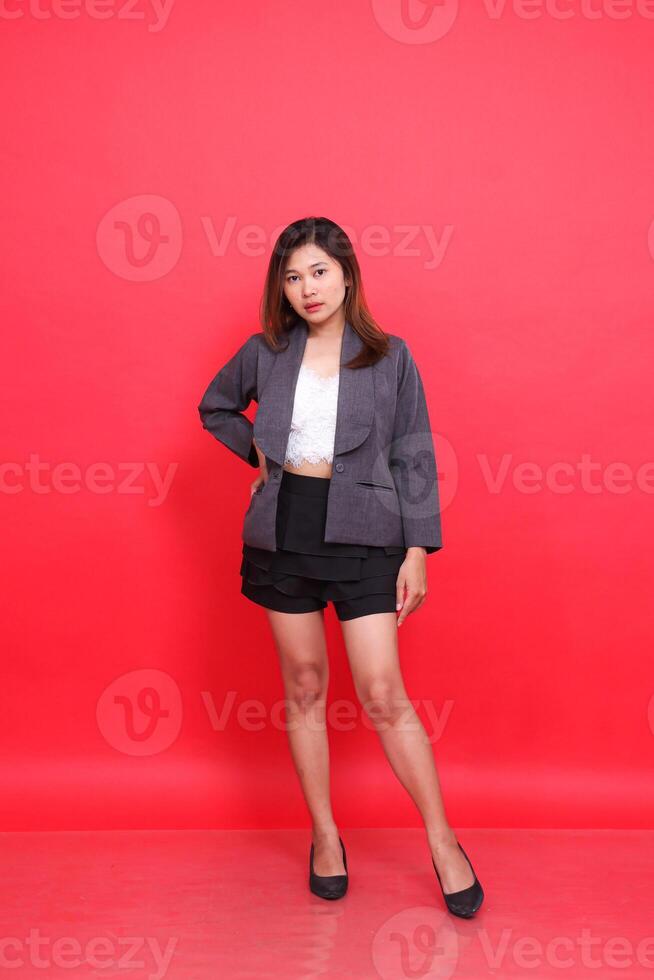 indonesia female executive in gray suit with long hair, white skin, photo in studio with red background standing holding waist. for corporate concepts, fashion and advertising