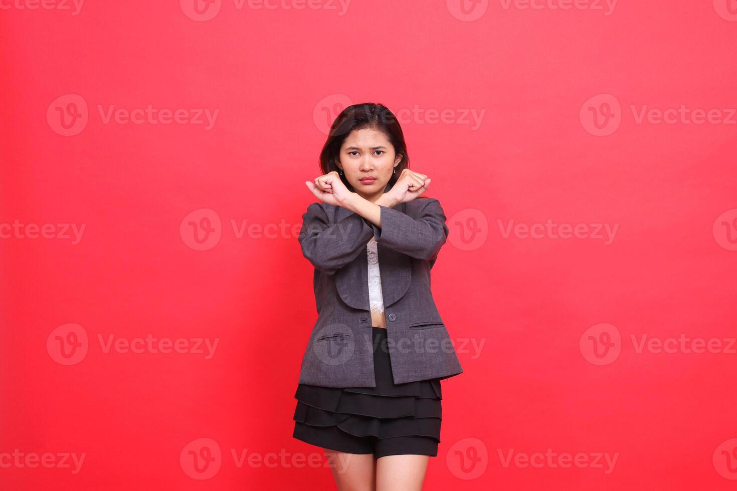 gesture of angry Asian office woman clenching both fists crossed as a stop sign wearing a gray jacket and mini skirt on a red background. for fashion, lifestyle and business concepts photo
