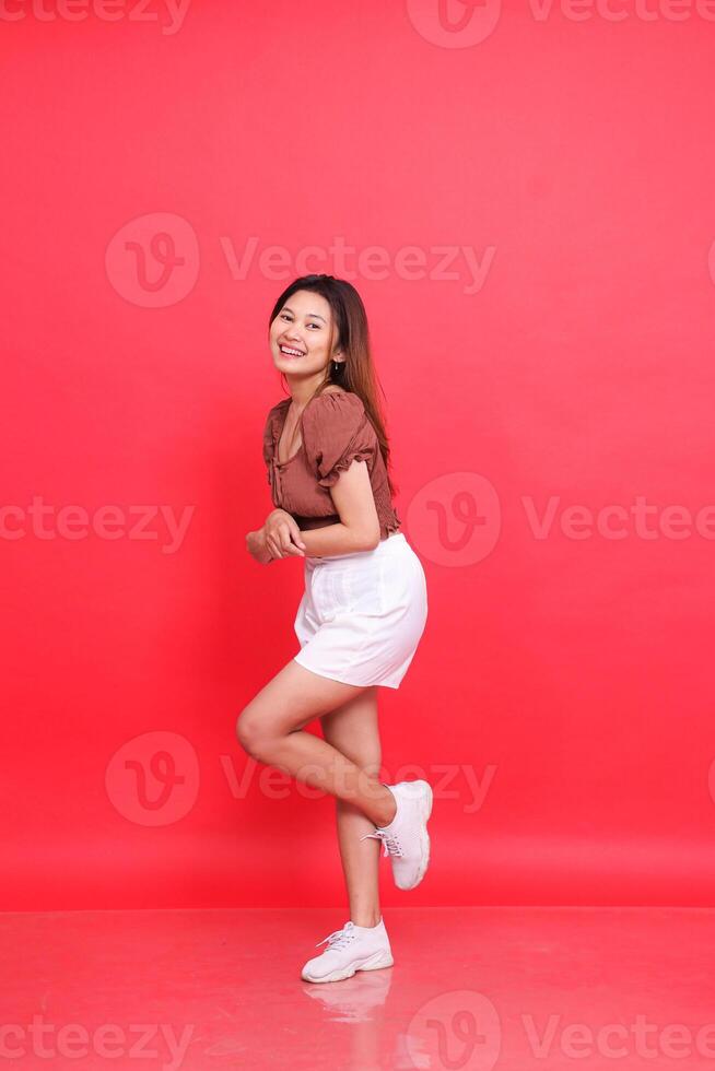 The elegance of a cheerful indonesia woman has her arms and legs crossed in front of her, wearing a brown blouse and shorts with a red background. for fashion, lifestyle and clothing concepts photo