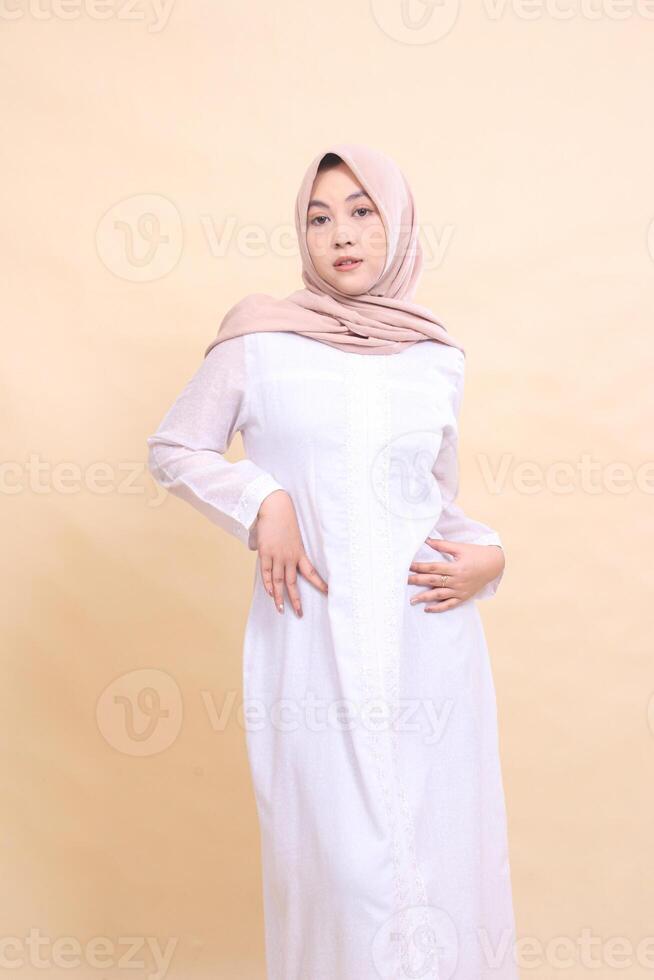 Asian woman wearing beautiful elegant muslim dress poses both hands to waist isolated on cream background - beauty, model, studio and fashion concept photo