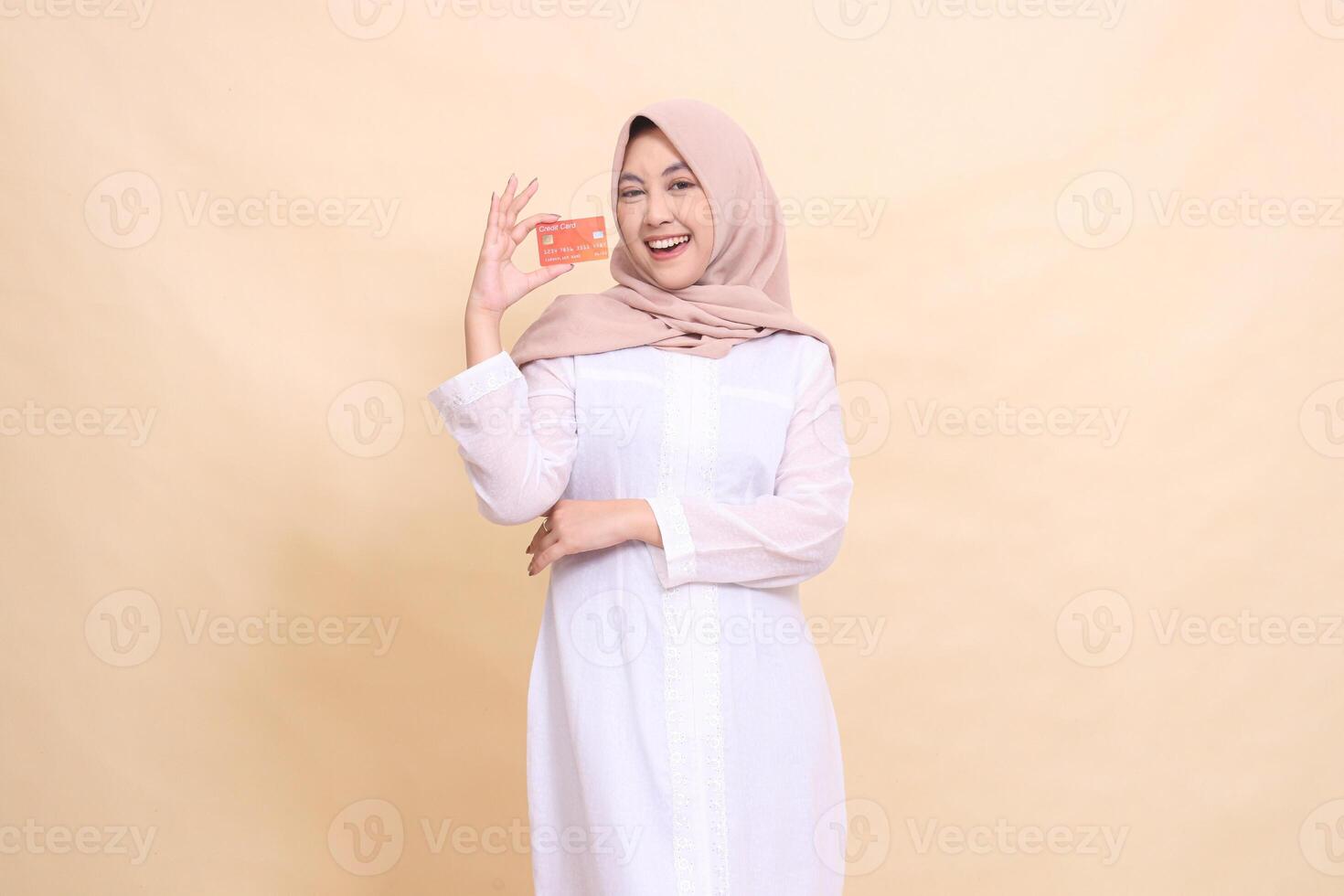 Muslim woman indonesia in hijab smiling cheerfully holding debit credit card in hand with arms crossed. Lifestyle, business and finance concept photo