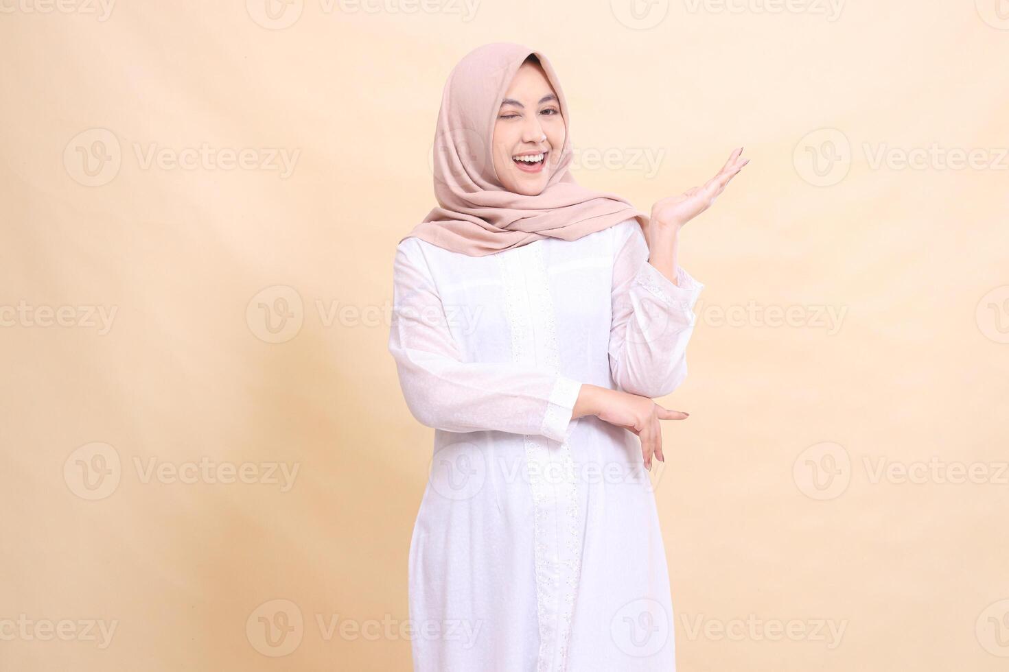 girl asian muslim standing to the camera smile cheerful wink eyes crossed arms presenting to the left. Fashion, pointer, business and promotion concept photo