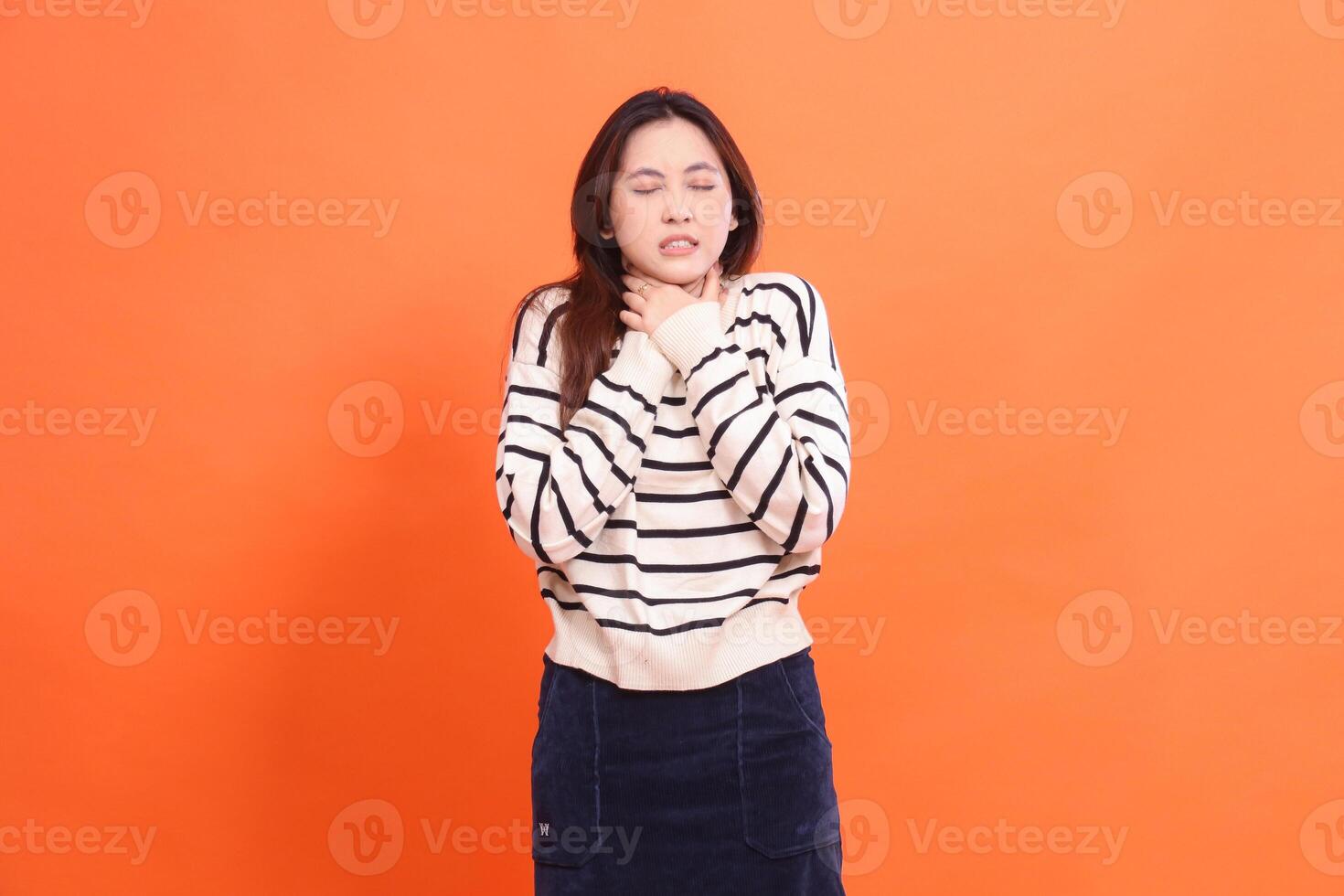 Beautiful mature asian woman closing eyes suffering from pain in neck after consuming food and drink isolated on orange background photo