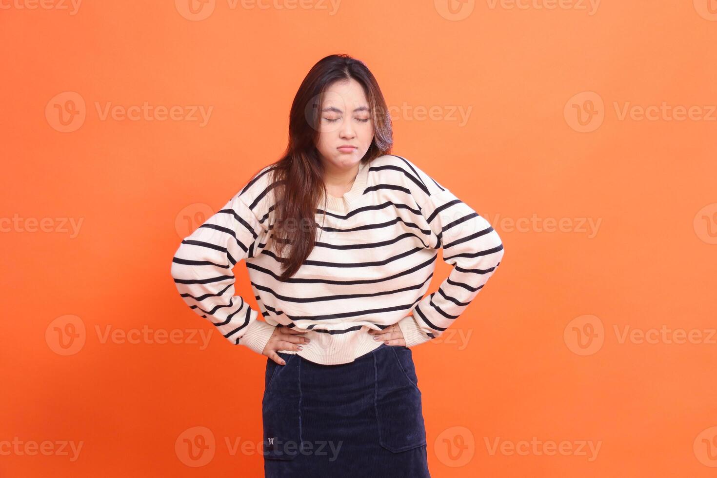 Stomach Pain Gesture Beautiful Young Asian Woman Wearing White Shirt Isolated on Orange Background. for health, care, solutions and stomach tips photo