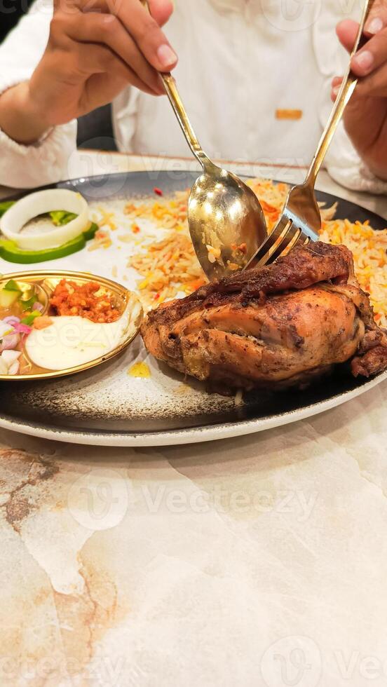 portrait of asian woman's hands slicing chicken with spoon and fork on a plate of nasi kebuli rice kebuli typical arabic food photo