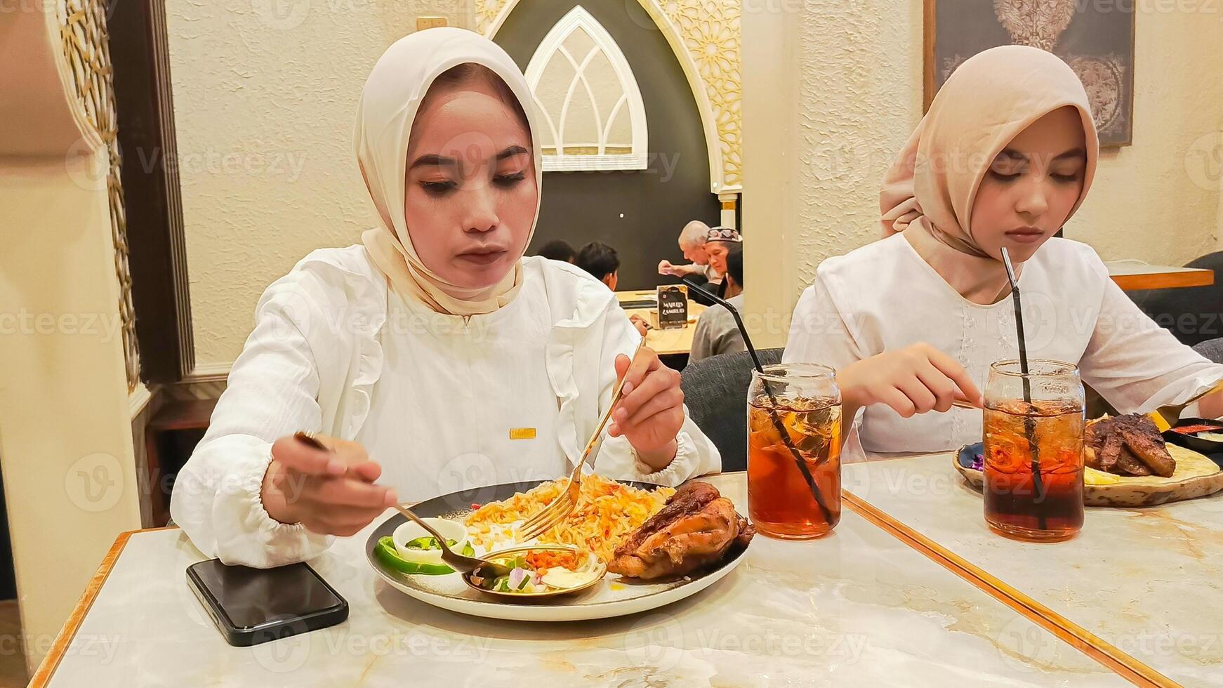 two women are enjoying a meal of kebuli rice and dajaj mashwi oven-roasted chicken and pita bread complete with drinks photo