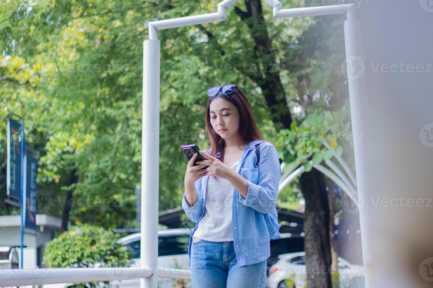 Beautiful Asian woman using smart phone gadget glasses in campus park on sunny summer day. female student for education, promotion and lifestyle concept photo