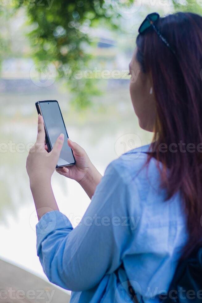 Beautiful Asian woman typing whatsapp message using gadget smart phone in campus park on sunny summer day. female students for education, promotion and lifestyle concepts photo