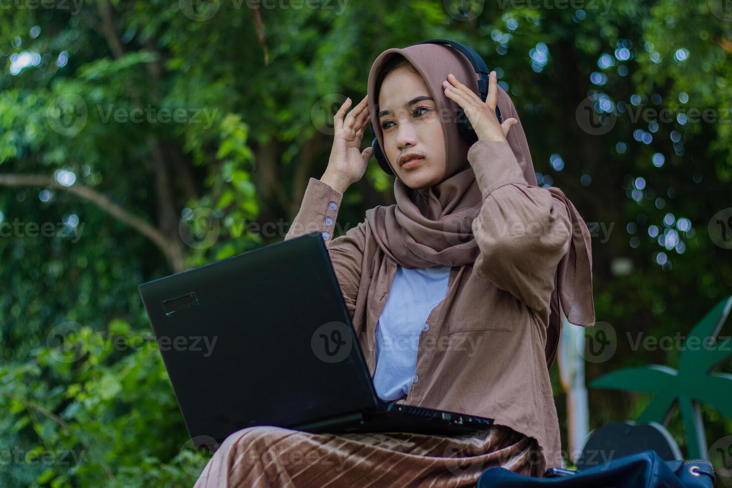 gesture Asian woman in hijab suffering from headache while sitting in outdoor park. female students for the themes of education, technology and health photo