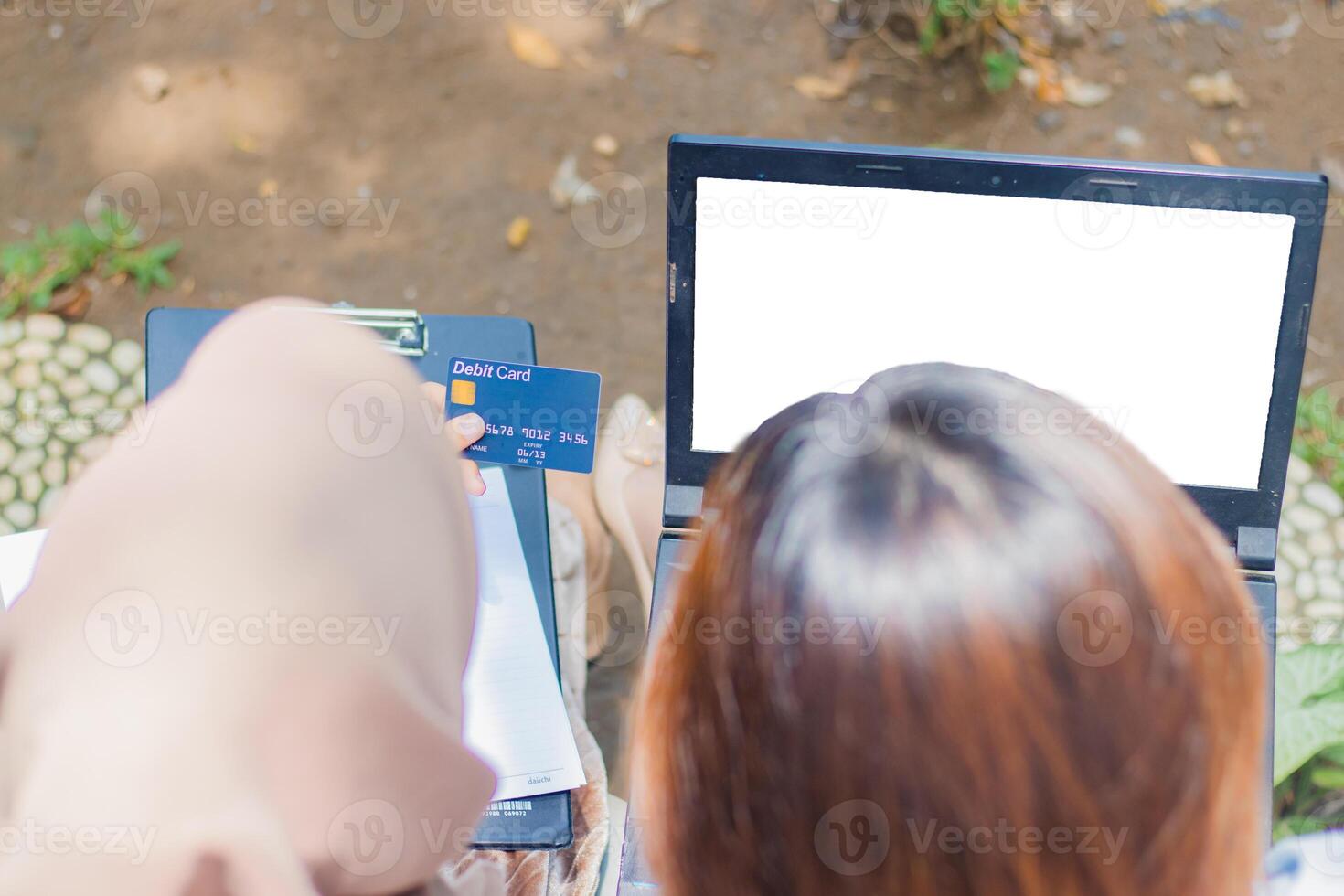 A pair of Asian women input credit card numbers to get discounts on online shopping by holding pens, books and clipboards in the campus park. female students for promotion and lifestyle concepts photo