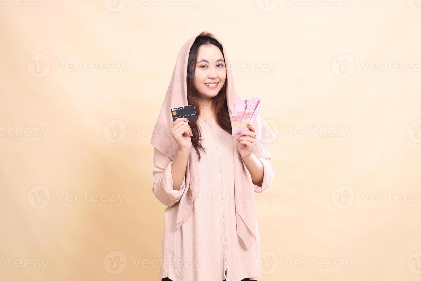woman indonesia with a cheerful smiling expression at the camera holding a debit card and carrying rupiah money. young beautiful for finance, advertising, fashion photo