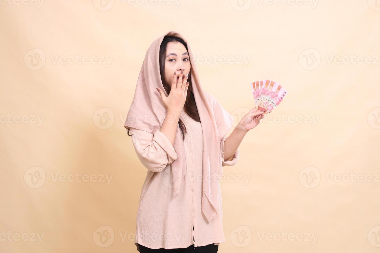 Asian woman shocked at the camera hands covering her mouth and carrying rupiah money. young beautiful for finance, advertising, fashion photo