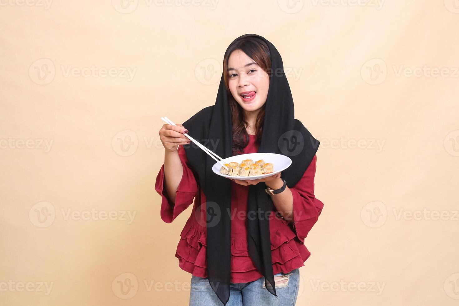Beautiful mature indonesia woman wearing a red hijab with a delicious expression, picking up with chopsticks and carrying a plate containing dimsum Chinese food. used for health content photo