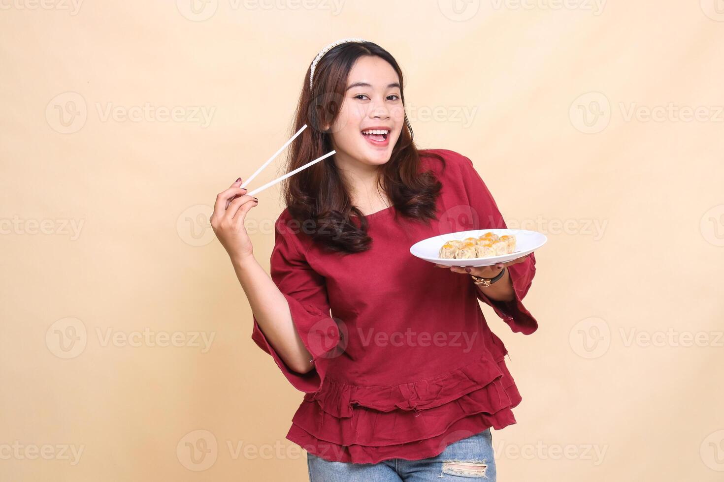 Beautiful Asian woman in red, smiling cheerfully, carrying a plate containing dim sum Chinese food and sauce with chopsticks to the side. used for food, health and lifestyle content photo