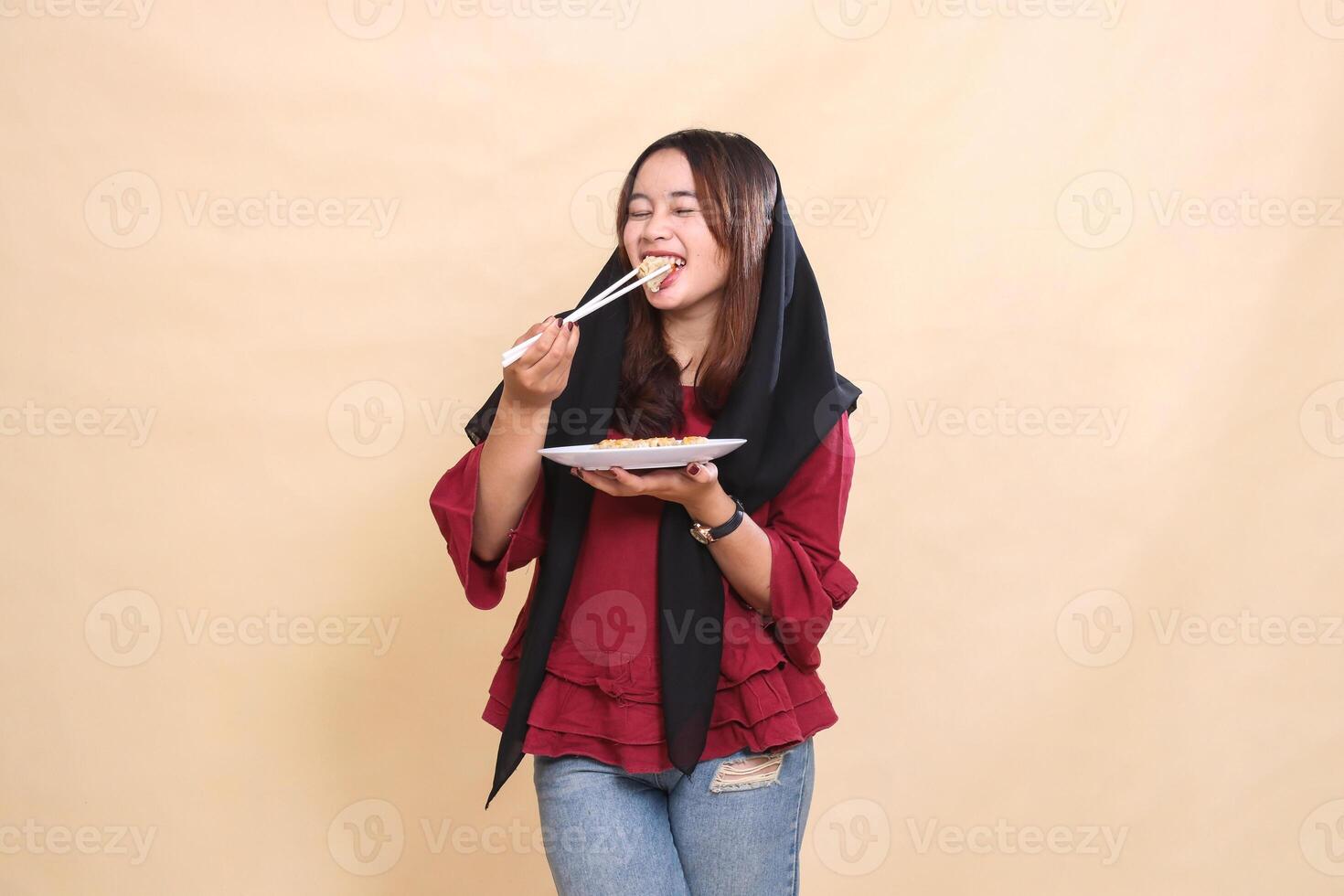 Beautiful mature Asian woman wearing a red headscarf eating dimsum with chopsticks and carrying a plate containing dimsum Chinese food to the front. used for food, health and culinary content photo