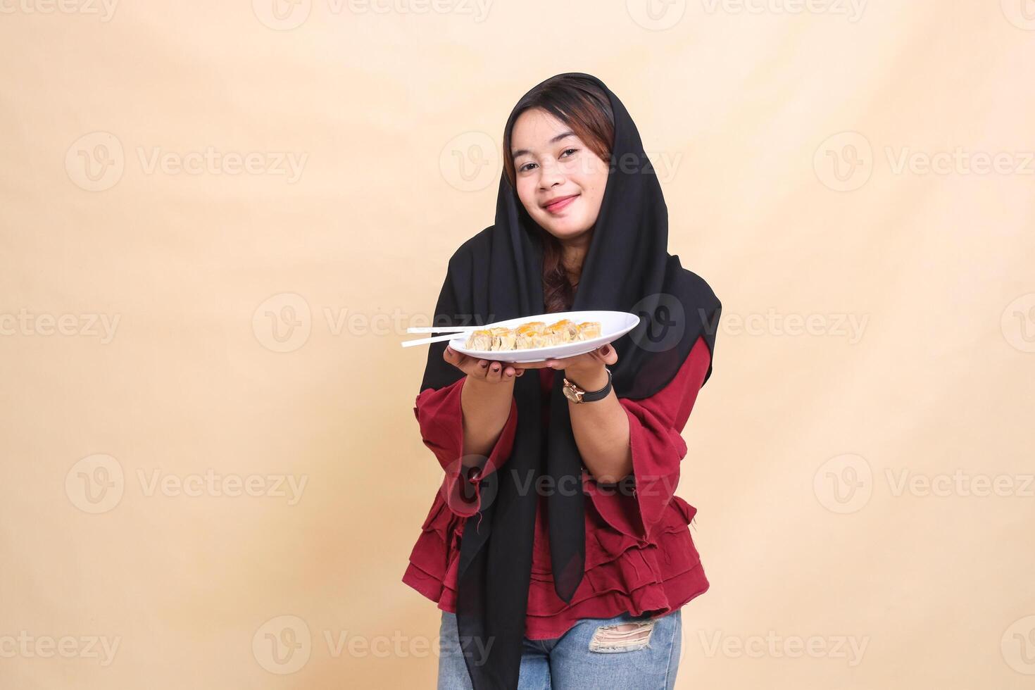 Beautiful mature Asian girl wearing a red hijab wearing a smile carrying a plate containing chopsticks and dimsum Chinese food in both hands. used for food, health and lifestyle content photo
