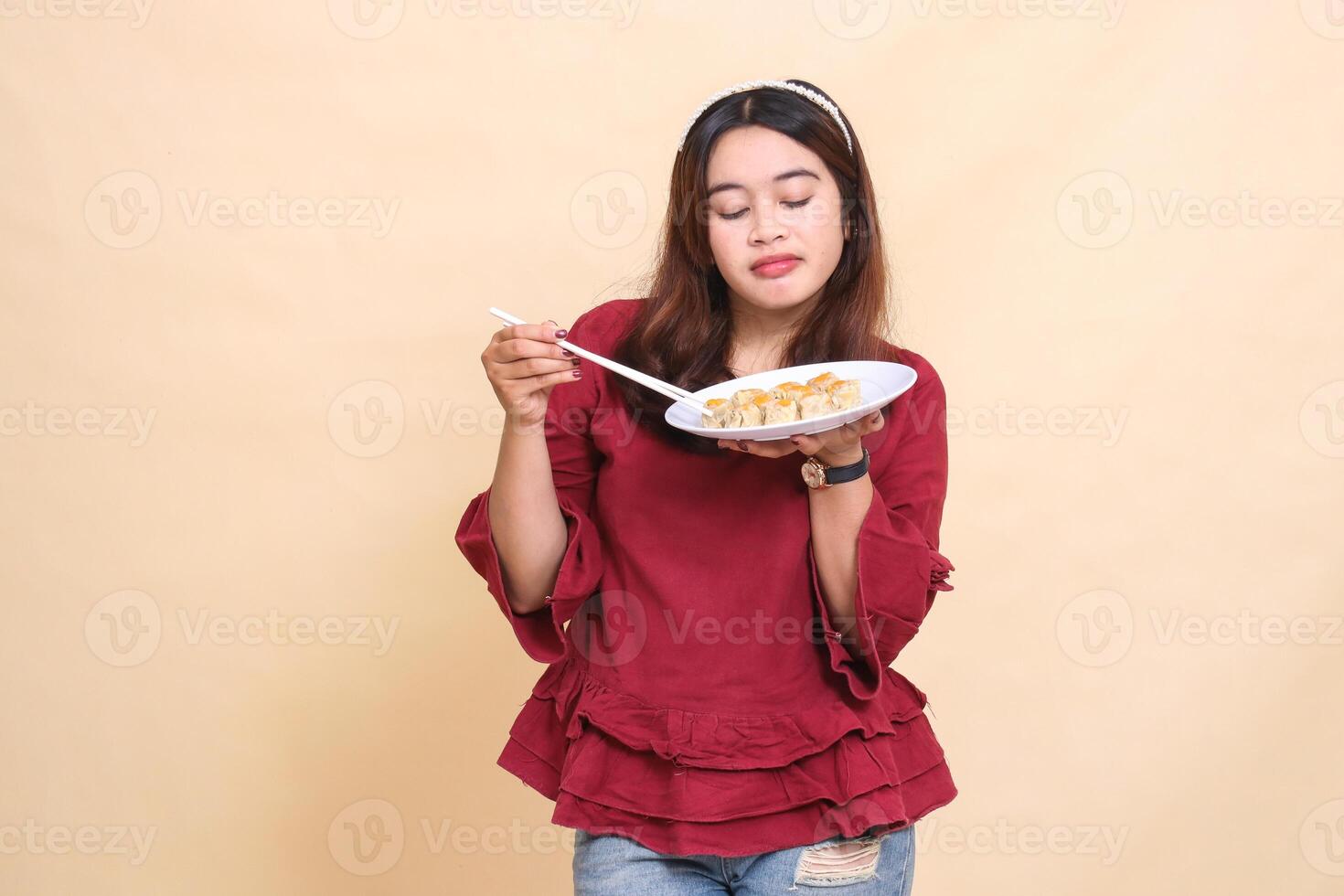 beautiful young indonesia woman in red pouting lifting a plate containing dimsum chinese food and sauce with chopsticks down picking it up. used for food, health and lifestyle content photo