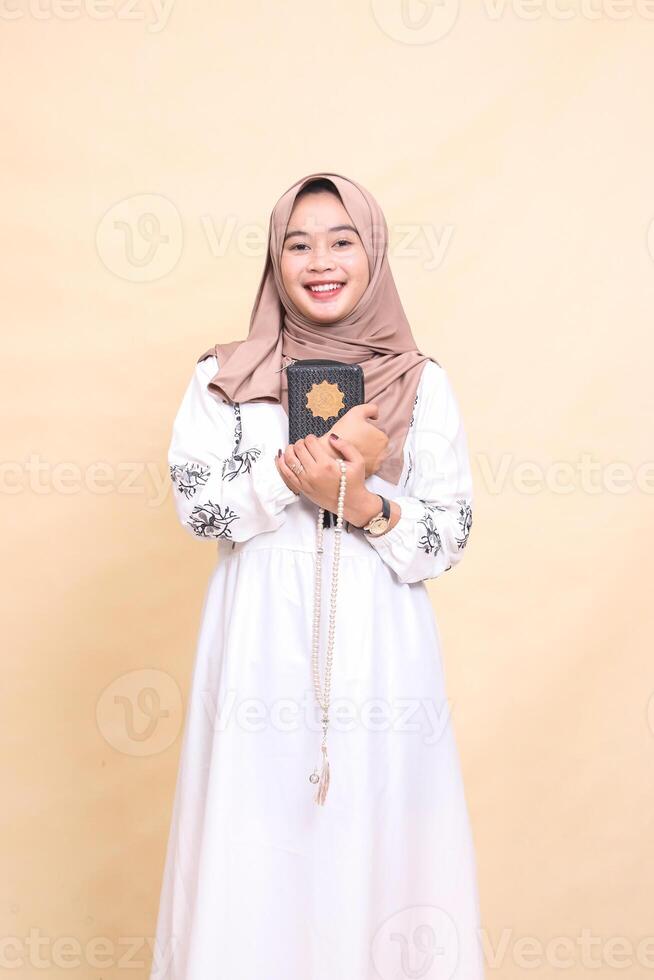 beautiful mature Asian Muslim woman in hijab smiling cheerfully hugging quran and holding prayer beads. for advertising, lifestyle, banners and Ramadan photo