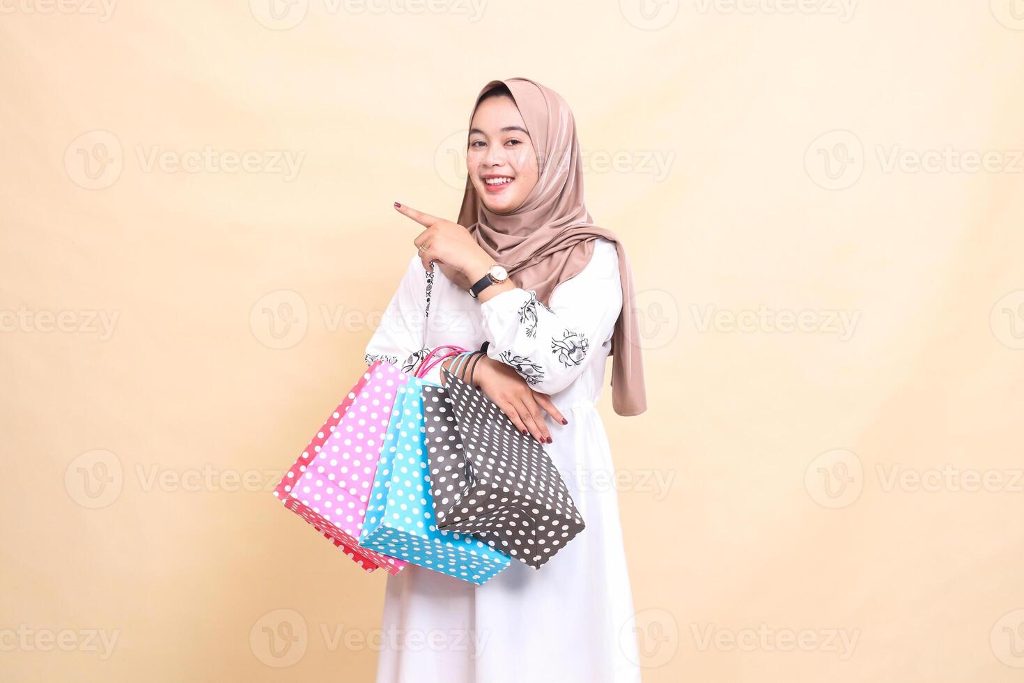 the story of a young Asian Muslim woman wearing a cheerful hijab pointing to the right and carrying a paperbag shopping bag. for advertising, culture, Eid and Ramadan photo