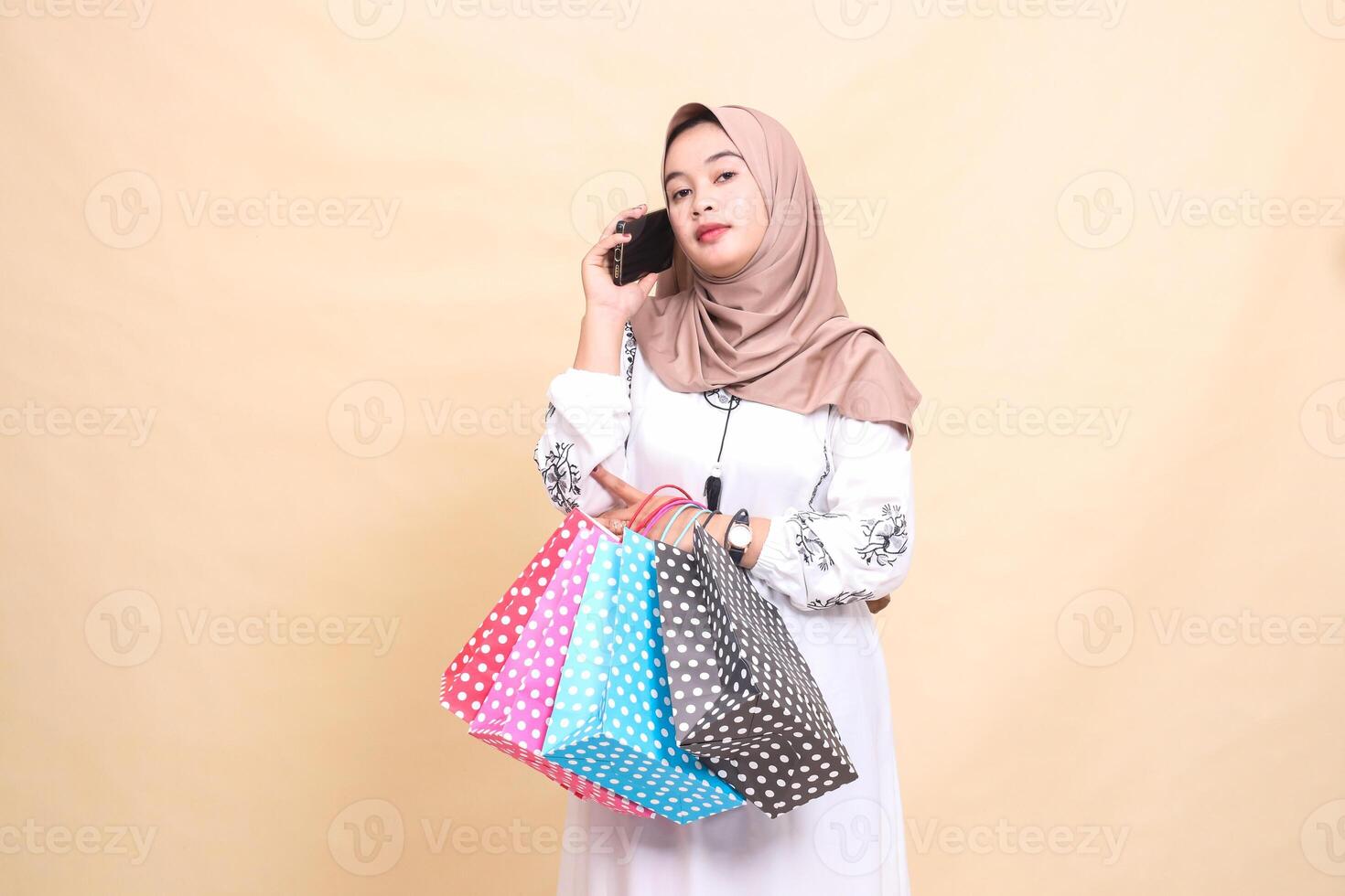 a young Asian Muslim woman in a hijab people's phone looking at the camera and carrying a paperbag shopping bag. for advertising, technology, Eid and Ramadan photo