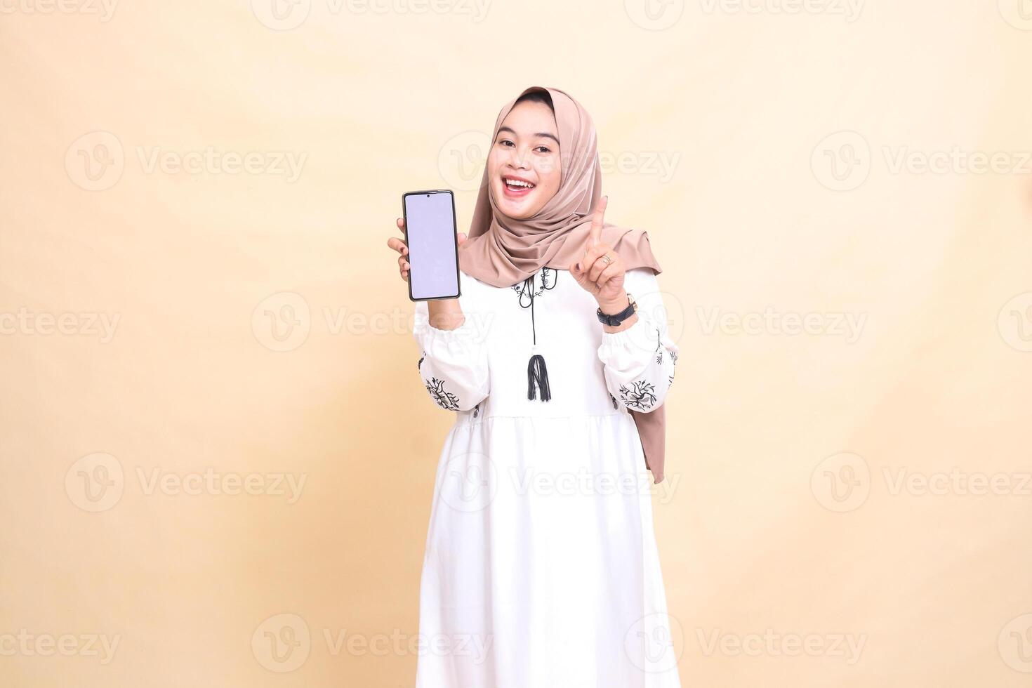 an adult indonesia Muslim woman wearing a hijab with a cheerful smile displays a cellphone gadget screen indicating how to create sales content. for advertising, technology, Eid and Ramadan photo